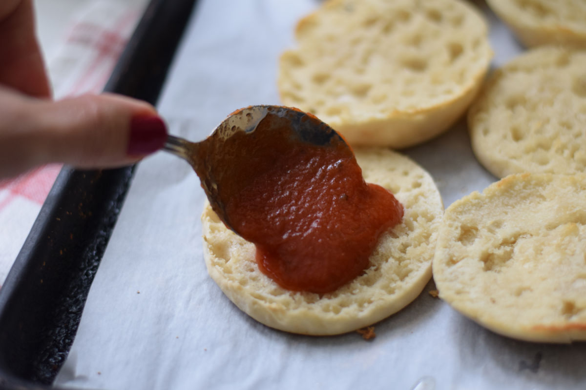 spooning pizza sauce on English muffins 